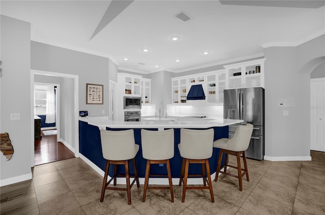 kitchen with a peninsula, arched walkways, stainless steel appliances, custom range hood, and white cabinetry