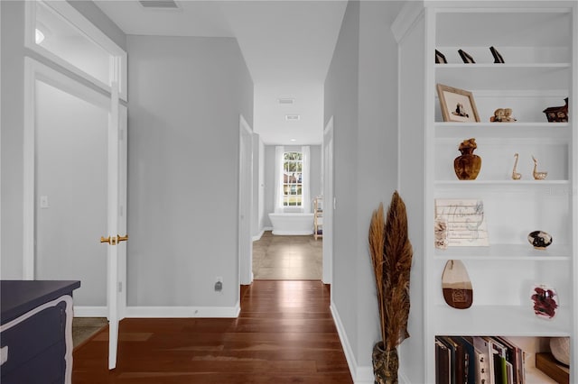 hallway with dark wood-style floors, visible vents, built in shelves, and baseboards