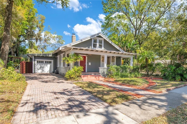 view of front of home with decorative driveway, a garage, a porch, and a chimney