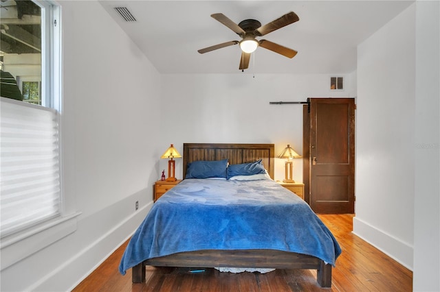 bedroom featuring a ceiling fan, wood finished floors, visible vents, and baseboards