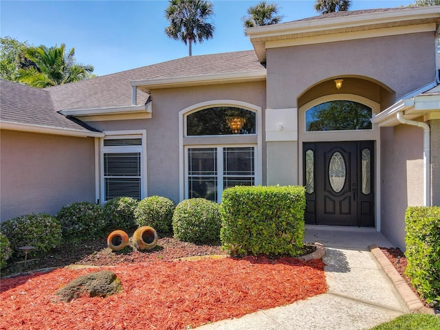 view of exterior entry featuring stucco siding and roof with shingles