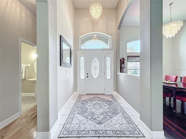 foyer with light wood-type flooring, arched walkways, an inviting chandelier, baseboards, and a towering ceiling