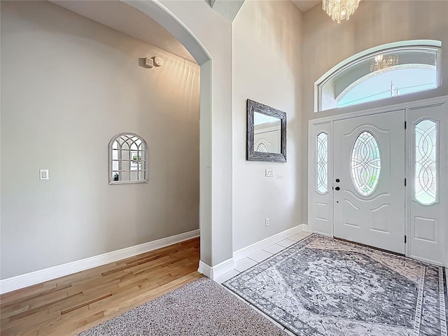 entrance foyer with baseboards, light wood-type flooring, a high ceiling, an inviting chandelier, and arched walkways