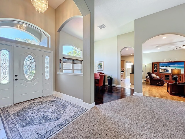 carpeted foyer with visible vents, baseboards, arched walkways, and wood finished floors