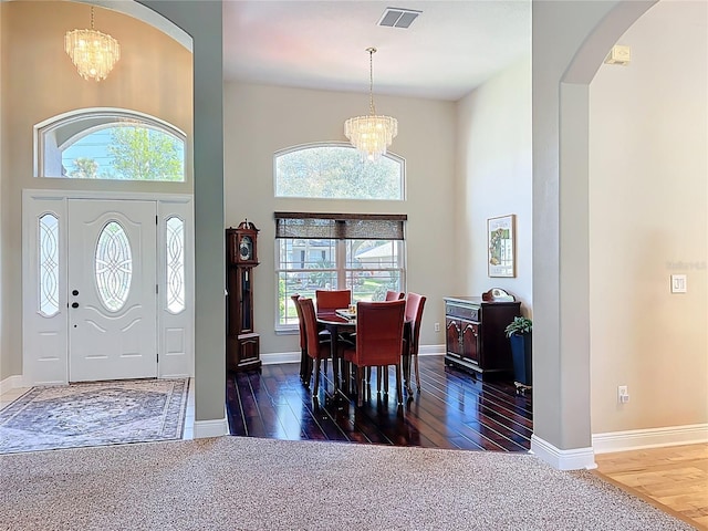 entryway featuring visible vents, a chandelier, a towering ceiling, wood finished floors, and arched walkways