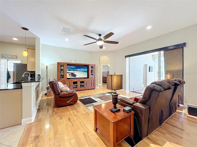 living area featuring light wood-type flooring, visible vents, a ceiling fan, recessed lighting, and arched walkways