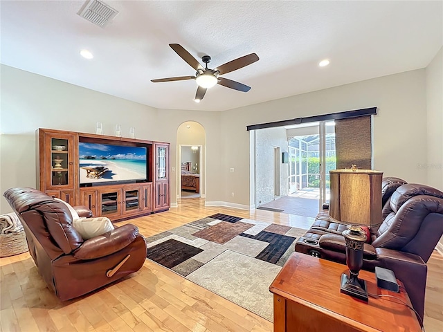 living room featuring a ceiling fan, baseboards, visible vents, arched walkways, and light wood-type flooring