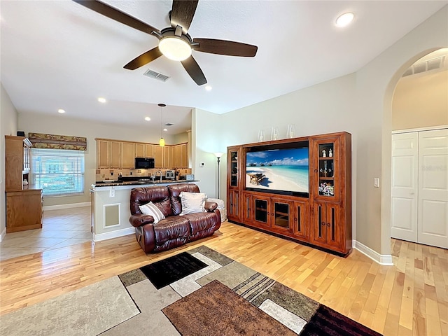 living area featuring arched walkways, visible vents, light wood-style flooring, and a ceiling fan