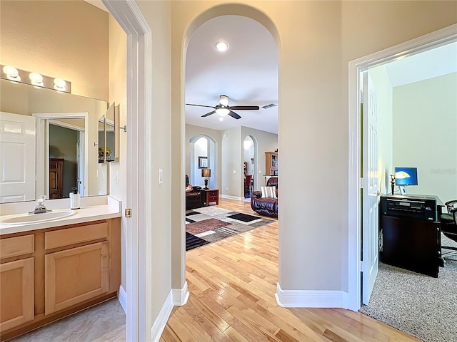 hall with visible vents, a sink, arched walkways, light wood-style floors, and baseboards