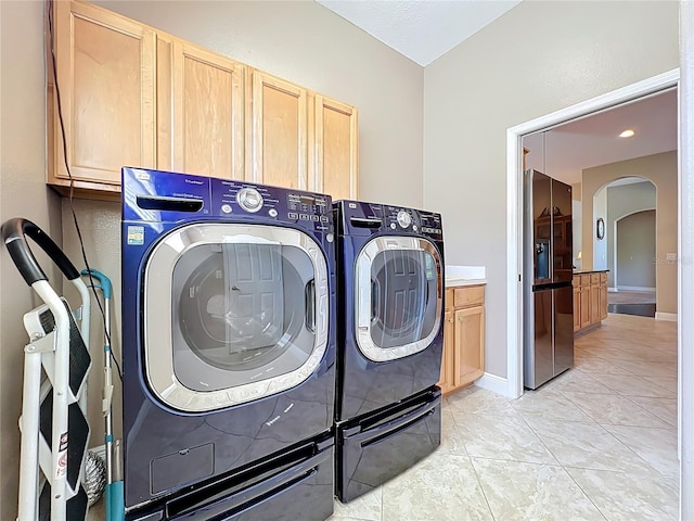 clothes washing area with light tile patterned floors, baseboards, cabinet space, arched walkways, and washer and clothes dryer