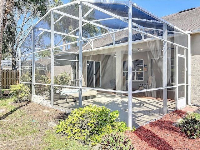 rear view of house featuring stucco siding, a patio, fence, a shingled roof, and a lanai