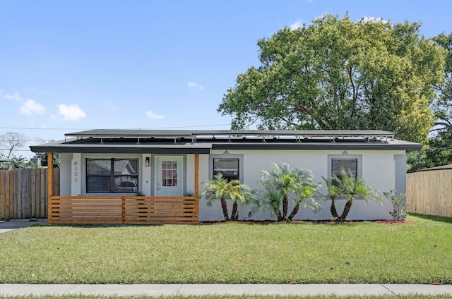 view of front of home featuring solar panels, a front lawn, fence, and stucco siding