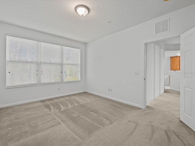 unfurnished room featuring a textured ceiling, light colored carpet, visible vents, and baseboards