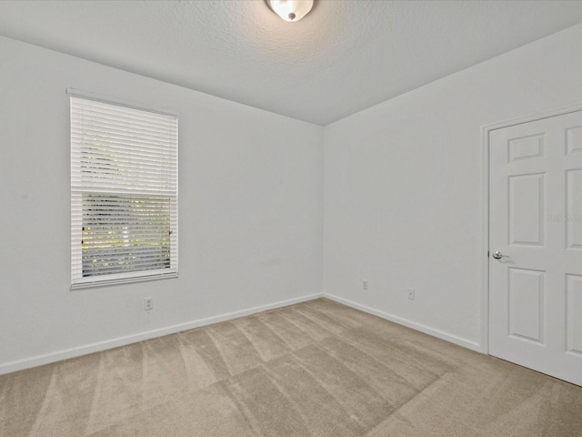 spare room with baseboards, light carpet, and a textured ceiling