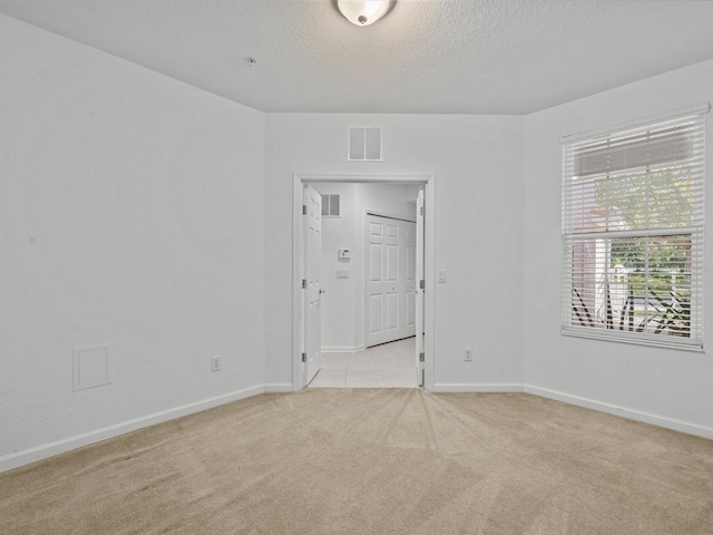 unfurnished room featuring visible vents, light colored carpet, a textured ceiling, and baseboards