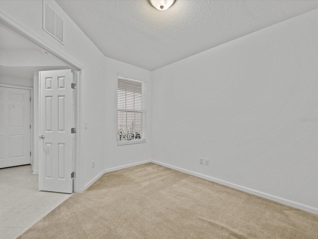 spare room featuring visible vents, light colored carpet, a textured ceiling, and baseboards