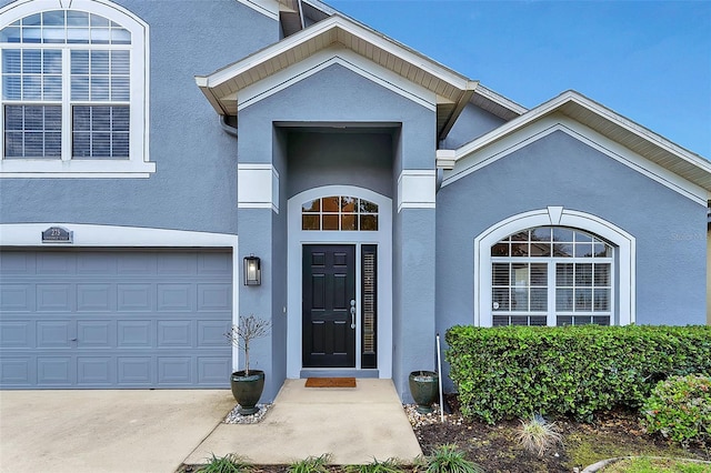 doorway to property with stucco siding, driveway, and an attached garage