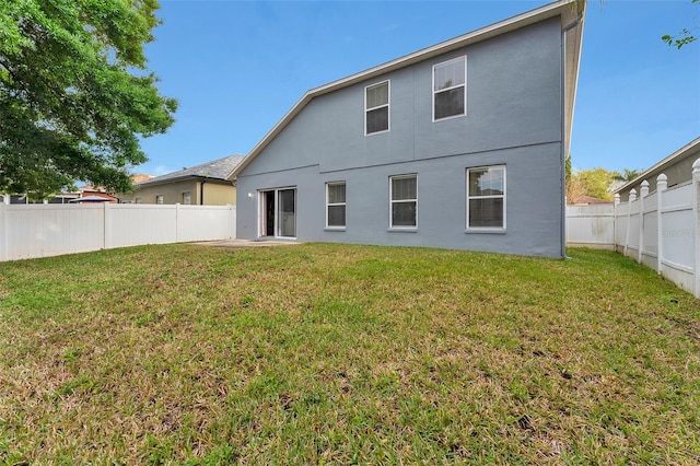 back of house with a yard, a fenced backyard, and stucco siding