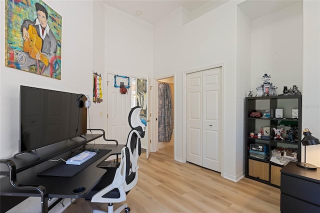 office space with baseboards, light wood-type flooring, and a high ceiling