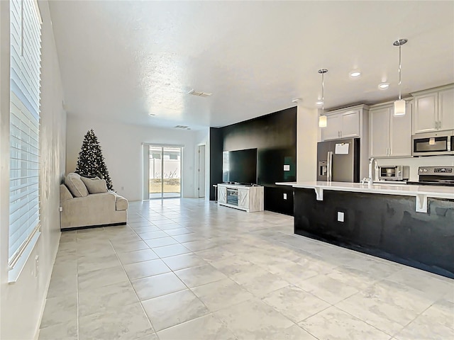 kitchen featuring open floor plan, pendant lighting, a kitchen bar, light countertops, and stainless steel appliances