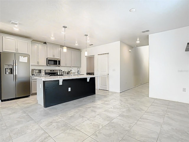 kitchen featuring visible vents, light countertops, a kitchen bar, appliances with stainless steel finishes, and a kitchen island with sink