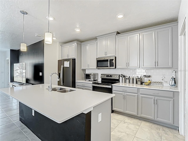 kitchen with an island with sink, a sink, stainless steel appliances, light countertops, and decorative light fixtures