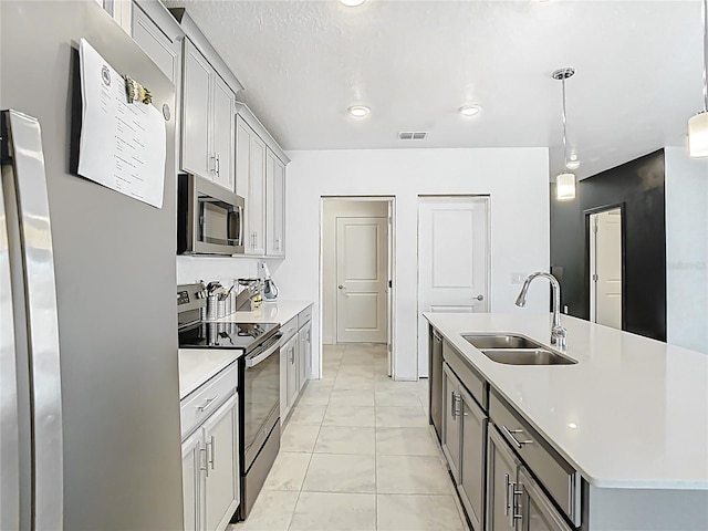 kitchen featuring visible vents, an island with sink, a sink, stainless steel appliances, and light countertops