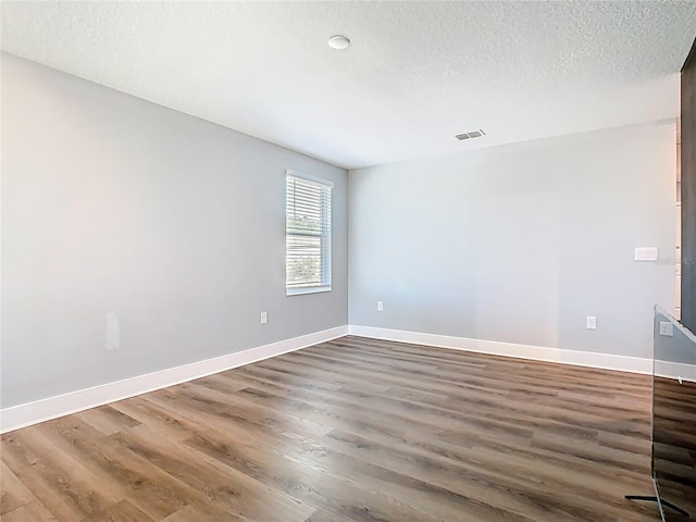 unfurnished room featuring baseboards, wood finished floors, visible vents, and a textured ceiling