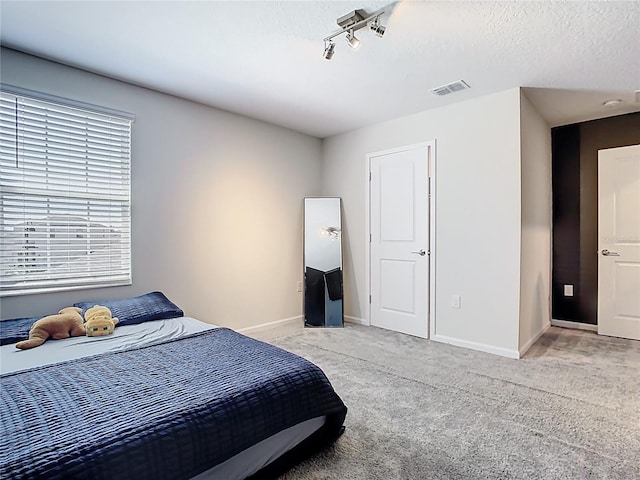 bedroom with baseboards, light carpet, a textured ceiling, and visible vents