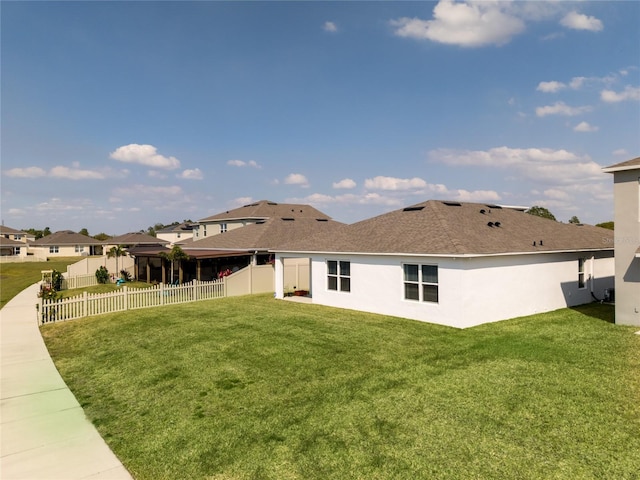 rear view of house with roof with shingles, a lawn, a fenced backyard, and stucco siding