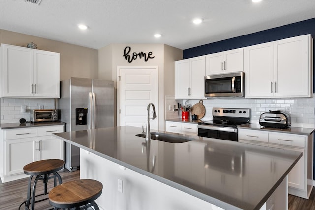 kitchen featuring dark countertops, dark wood-type flooring, a kitchen bar, appliances with stainless steel finishes, and a sink