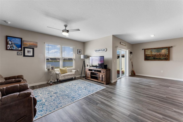 living room featuring wood finished floors, a ceiling fan, baseboards, and a textured ceiling