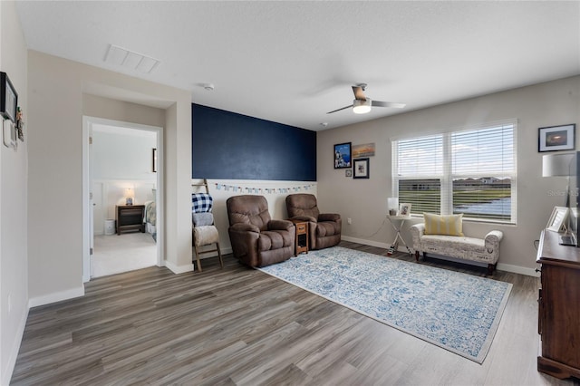 living area with visible vents, baseboards, wood finished floors, and a ceiling fan