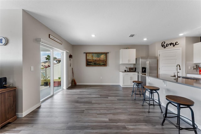 kitchen with a kitchen bar, white cabinets, wood finished floors, stainless steel fridge, and a sink