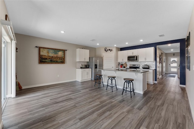 kitchen with a kitchen bar, backsplash, light wood-type flooring, and appliances with stainless steel finishes