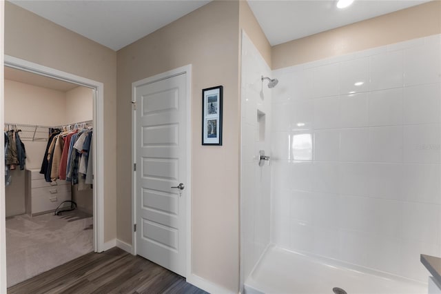 bathroom with tiled shower, a walk in closet, baseboards, and wood finished floors