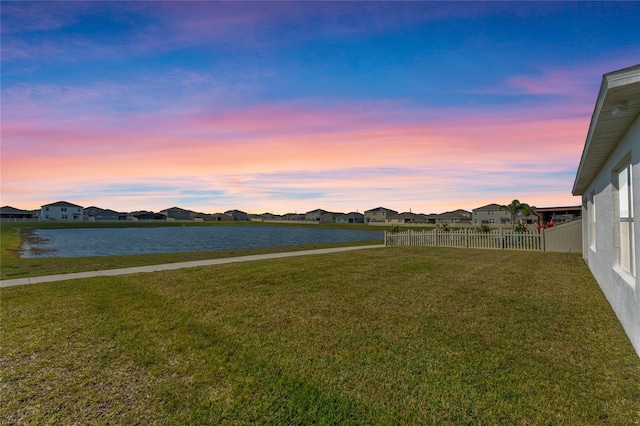 yard at dusk with a residential view, fence, and a water view