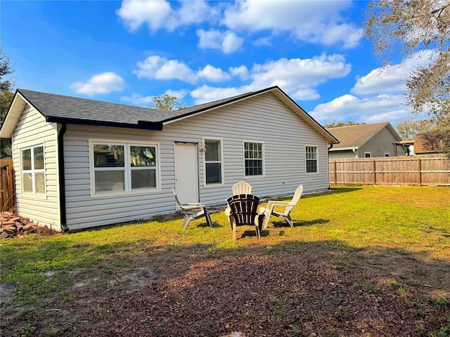 rear view of house with a lawn, a shingled roof, and fence