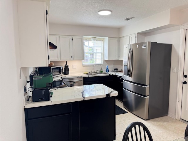 kitchen featuring a peninsula, a sink, light countertops, appliances with stainless steel finishes, and white cabinetry