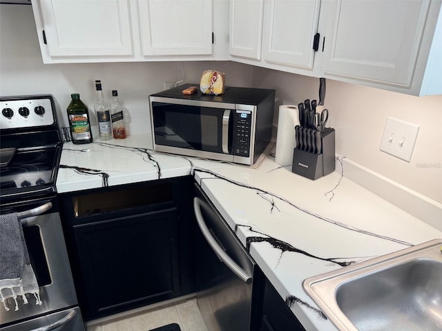 kitchen featuring a sink, light stone counters, white cabinetry, appliances with stainless steel finishes, and light tile patterned flooring