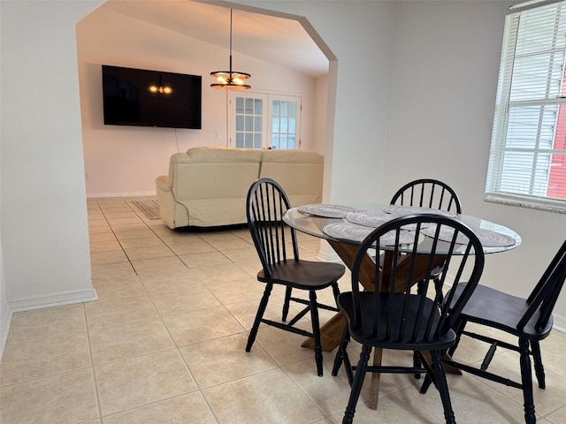 dining space with vaulted ceiling, light tile patterned floors, baseboards, and arched walkways