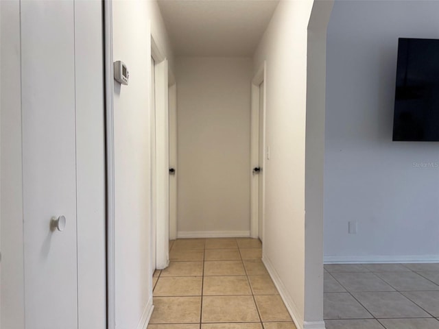 corridor featuring light tile patterned floors, baseboards, and arched walkways