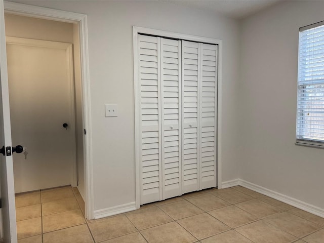 unfurnished bedroom featuring light tile patterned flooring, baseboards, and a closet