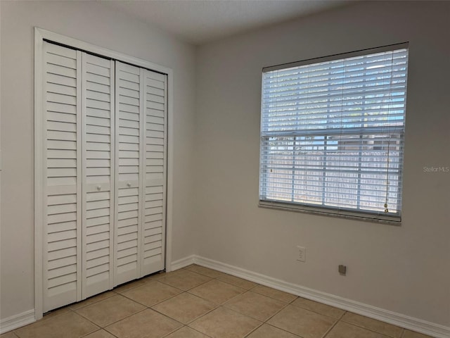 unfurnished bedroom with light tile patterned floors, baseboards, and a closet