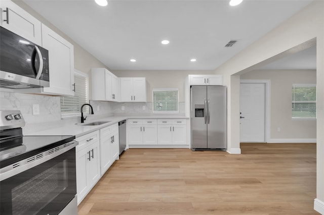 kitchen with a sink, stainless steel appliances, light wood-style flooring, and white cabinetry