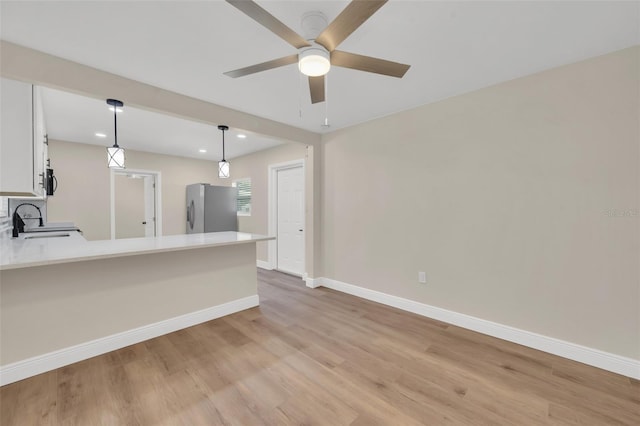 kitchen with a sink, stainless steel fridge, a peninsula, baseboards, and ceiling fan