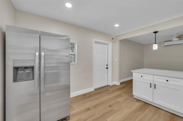 kitchen with baseboards, a wall mounted AC, light wood-style flooring, stainless steel fridge with ice dispenser, and white cabinetry