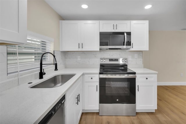 kitchen featuring backsplash, light wood-style flooring, appliances with stainless steel finishes, white cabinets, and a sink