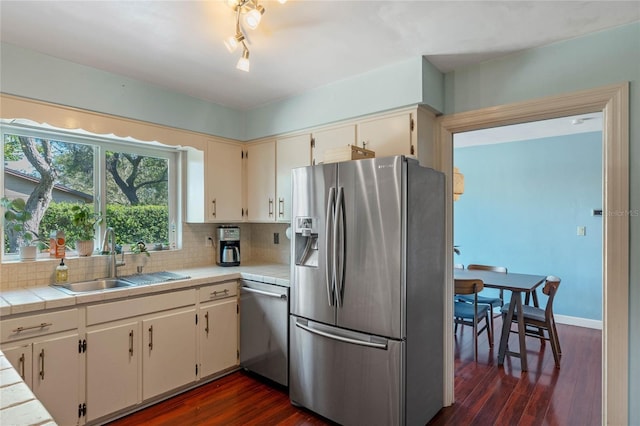 kitchen with backsplash, dark wood finished floors, appliances with stainless steel finishes, cream cabinetry, and a sink