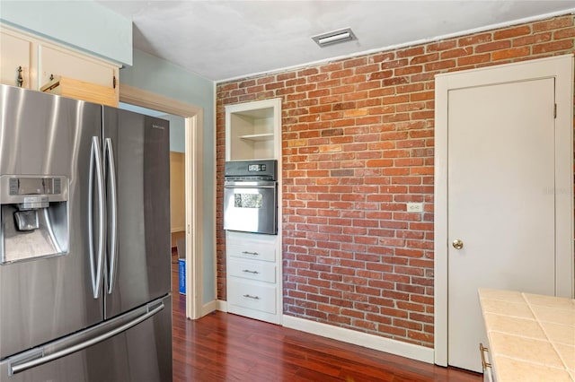 kitchen featuring oven, visible vents, dark wood-type flooring, tile countertops, and stainless steel fridge